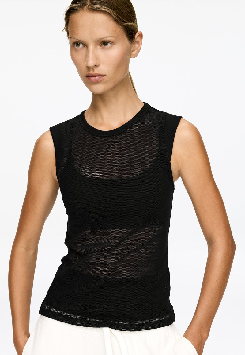 Top sans manches noir avec un design en maille transparente et un col rond, présentant un tissu texturé et une silhouette ajustée.