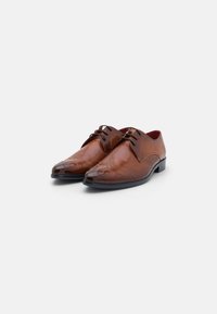Scarpe da uomo in pelle marrone con finitura liscia, punta affusolata, perforazioni decorative e suola scura a contrasto. Presentano lacci e cuciture sottili.