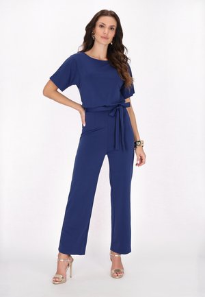 Tuta blu navy con maniche corte, vita con cintura, gamba ampia, texture liscia, abbinata a tacchi gold con cinturini.