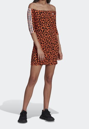 Kvinde iført en orange off-shoulder kjole med sort leopardprint og hvide striber på ærmerne, kombineret med sorte sportssko.