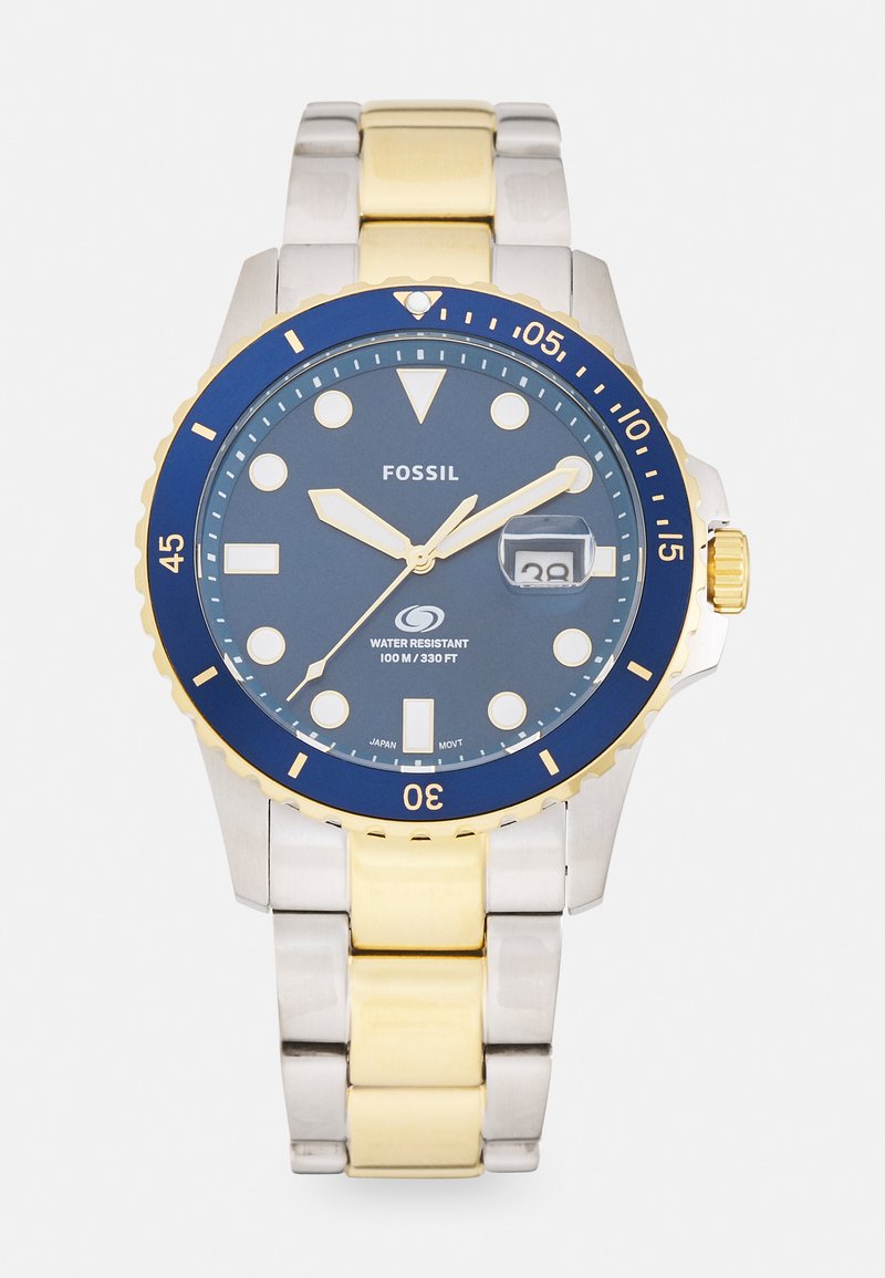 Montre Fossil avec un cadran bleu, des accents dorés, un bracelet en acier inoxydable, des marqueurs lumineux et un affichage de la date. Étanche jusqu'à 100 mètres.