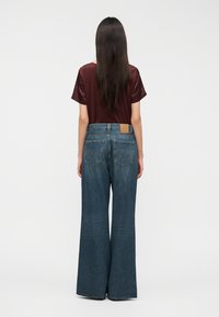 Τζιν σκούρου χρώματος με φαρδιά πόδια και ψηλή μέση, με πίσω τσέπες και δερμάτινο λογότυπο, συνδυασμένο με μπλούζα κοντομάνικη σε μπορντό χρώμα.