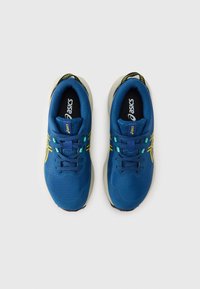 Blå joggesko med en strukturert overdel, gule detaljer og svarte såler. Har snøring og logo på tungen.