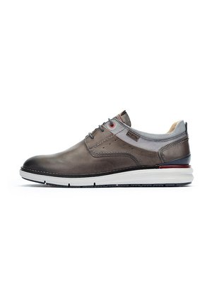 Zapato de cuero gris con acabado suave, puntera redonda, acentos de textil gris, detalles de ojal rojo y suela de goma blanca con relieve negro.