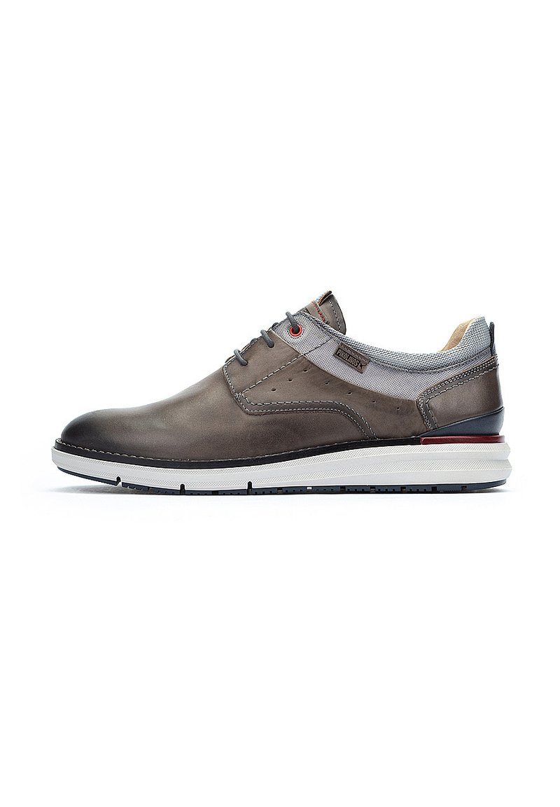 Zapato de cuero gris con acabado suave, puntera redonda, acentos de textil gris, detalles de ojal rojo y suela de goma blanca con relieve negro.