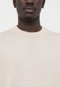 Sudadera de algodón color beige claro con cuello redondo, textura acanalada y corte ligeramente holgado, con detalles de costura mínimos.