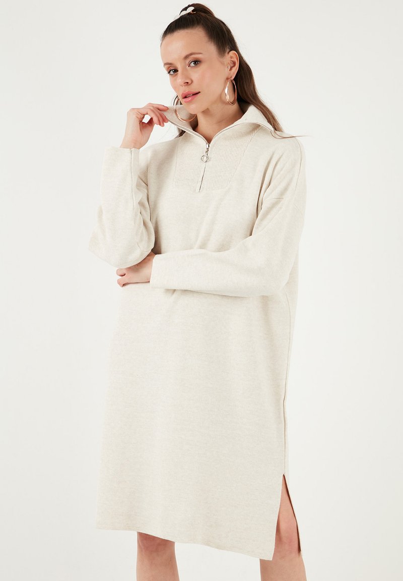 Langes beige Sweatshirtkleid mit Reißverschlusskragen, gerippter Textur am Kragen, seitlichen Schlitzen und langen Ärmeln. Aus weichem Stoff und mit lockerer Passform.