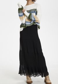 Suéter de punto en blanco con rayas azul, verde y ocre; combinado con una falda larga negra y fluida y botas beige con cordones.