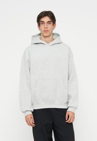 Siva hoodie izrađena od mekanog pamuka, koja ima kenguru džep, rebraste rukave i diskretan logo na prsima.