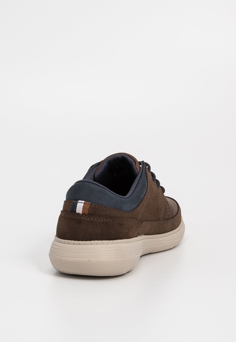 Zapatilla de ante marrón con acentos de tela azul, punta redonda, suela de goma beige y cordones marrones. Presenta un pequeño detalle de rayas en el talón.