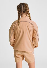 Peachfarvet træningssæt med en tekstureret langærmet jakke med reflekterende detaljer og matchende shorts.