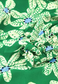 Groene stof met een bloemenpatroon met grote witte bloemen en blauwe centra. Het materiaal is zacht met een gerimpelde textuur en geplooide details.