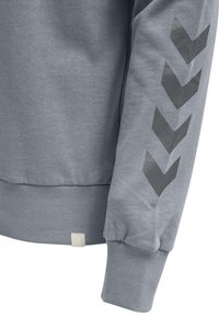 Sweatshirt gris avec poignets et ourlet côtelés. Présente un grand motif flèche en gris foncé sur la manche. Tissu à texture douce.