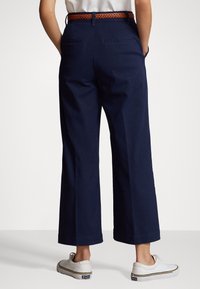 Marina vida byxor i brett snitt, tillverkade av bomull med ett texturerat brunt flätat bälte; har bakfickor och en ren fåll. Matchade med vita sneakers.