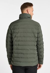 Pufferjack in donkergroen, met een gewatteerde textuur, hoge kraag en een getailleerd silhouet. Zachte, matte afwerking zonder zichtbare hardware.