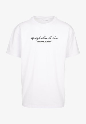 Witte ronde hals t-shirt met zwarte tekst waarop staat "Boven de chaos," "UPscale Studios," en "Art of Flight Lente/Zomer 23" aan de voorkant.