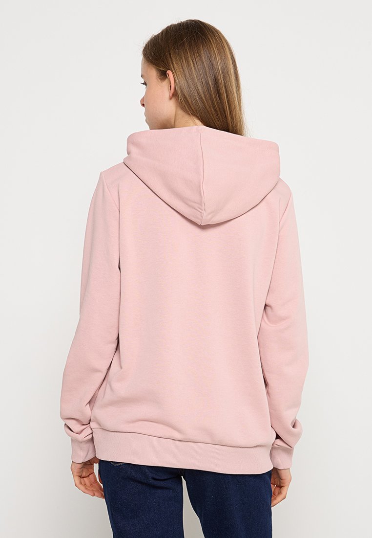 Roze hoodie gemaakt van zachte stof, met een ruime capuchon en ribbelboorden bij de mouwen en onderkant. Het ontwerp is eenvoudig, zonder zichtbare logo's of patronen.