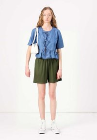 Denim peplum top s krátkymi rukávmi, modrej farby, s prednými viazaniami. Skombinované s olivovozelenými šortkami a bielymi teniskami, s malou bielou taškou.