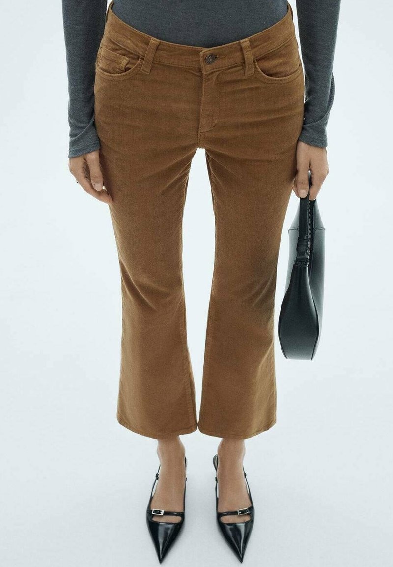 Pantalons en velours côtelé marron évasés avec une texture lisse, poches style denim et taille haute. Assortis à des escarpins noirs à bout pointu.