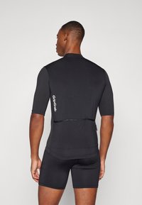 Maillot de cyclisme noir à manches courtes avec une coupe ajustée, doté d'accents en maille et d'une poche arrière pour le rangement. Logo visible sur le côté.