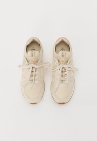 Beżowe sneakersy z teksturowanej tkaniny, gumowymi podeszwami, sznurowanym designem oraz kontrastującymi pastelowymi akcentami na języku i logo.