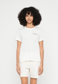 Bela bombažna majica s kratkimi rokavi in okroglim izrezom. Na sprednji strani ima natisnjen logotip "GANT 1949" v črni in rdeči barvi.