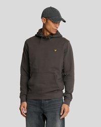 Haut à capuche gris foncé avec une poche kangourou, un capuchon à cordon, et un petit logo jaune sur la poitrine. Porté avec une casquette assortie et un jean.