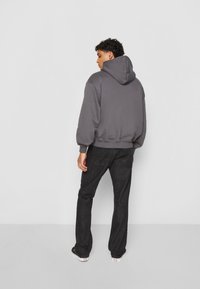 Grå hettegensere med snorhette, ribbad mansjetter og nederkant; paret med mørk denimjeans og svarte joggesko. Utsikt fra baksiden.