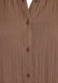 Brown button-up shirt, textured fabric with a slight sheen, featuring four small buttons down the front and a loose, relaxed fit.