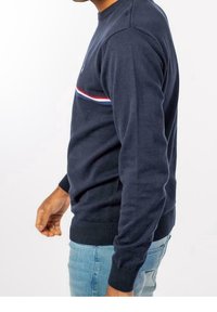 Suéter azul marino con cuello redondo, puños acanalados y dobladillo. Presenta una franja horizontal roja y blanca en el pecho.
