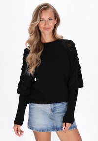 Czarny sweter z dzianiny z prążkowanymi długimi rękawami i fakturowanymi, pufowymi detalami na ramionach, zestawiony z jasnoniebieską spódnicą dżinsową.