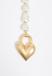 Pendente a forma di cuore in oro con lucchetto su una collana di perle irregolari e lucide di colore bianco. Il design è liscio con una finitura lucida.