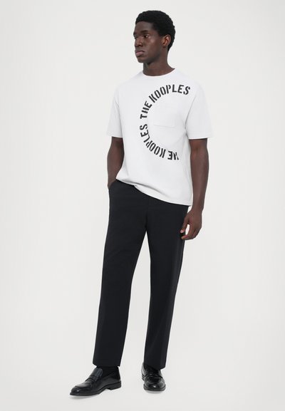 Tricou alb din bumbac cu text circular negru care spune "THE KOOPLE'S", asortat cu pantaloni negri �și mocasini negri. Design simplu și curat.