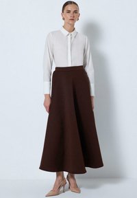 Brown, knee-length skirt with a flared design made from a soft material, paired with a white collared shirt and beige heels.
