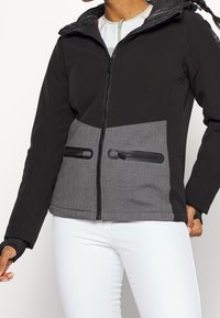 Czarna i szara kurtka zapinana na zamek z górną częścią w jednolitym kolorze i dolną częścią z wzorem, wyposażona w dwie kieszenie zapinane na zamek oraz kaptur. Miękka w dotyku.