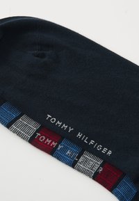 Chaussette marine jusqu'au genou avec un motif rayé multicolore à la cheville, avec le texte "TOMMY HILFIGER" tissé en blanc. Matériau en maille douce.