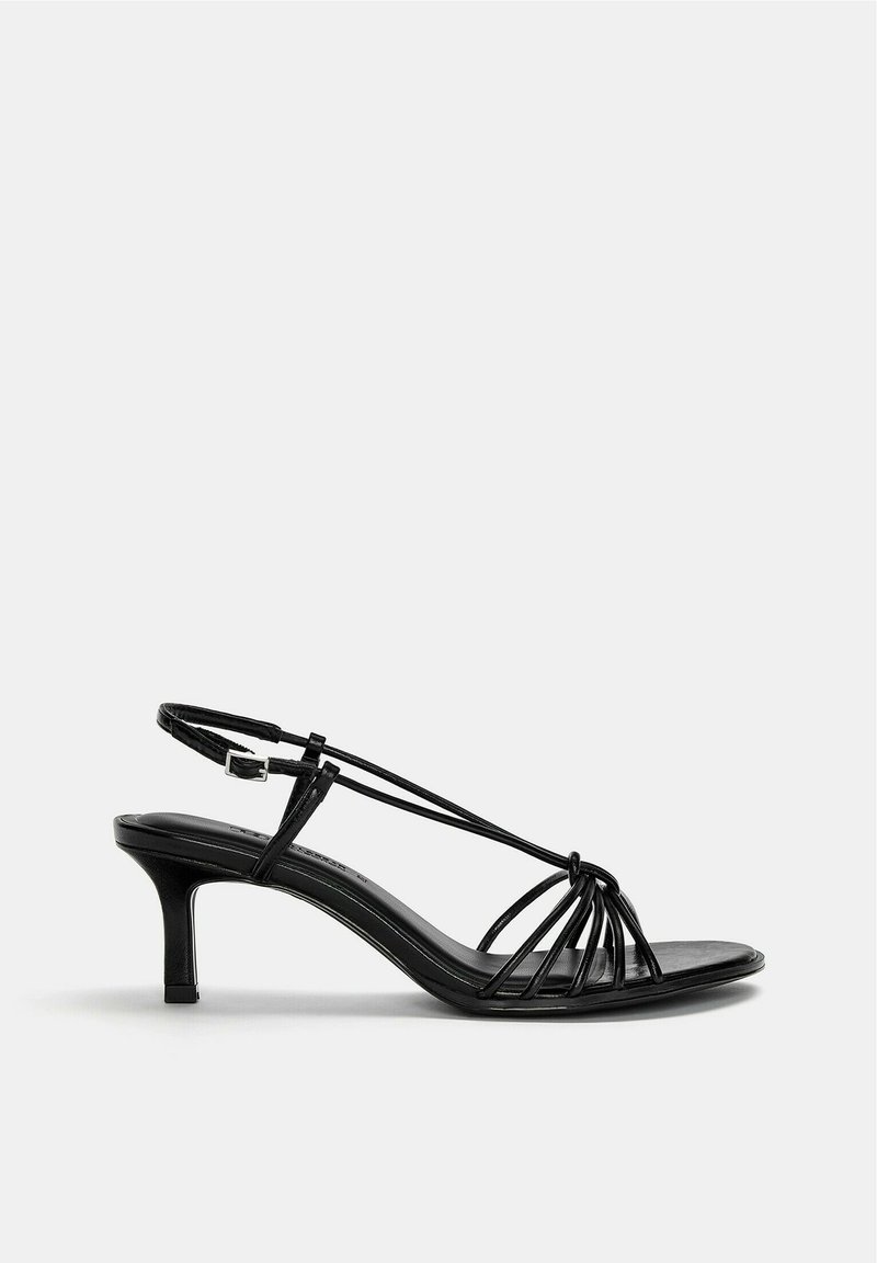 Sandalias negras de tacón con tiras delgadas, diseño de punta abierta y tacón fino. Presentan un detalle cruzado y una tira trasera ajustable con hebilla.