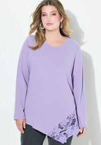 Lila Langarmshirt mit V-Ausschnitt und asymmetrischem Saum, der mit Spitzendetails am unteren Rand verziert ist. Weicher Stoff mit lockerem Sitz.