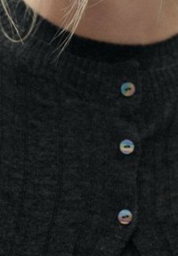 Cardigan en tricot gris foncé avec texture côtelée et quatre boutons ronds irisés le long de l'ouverture frontale.