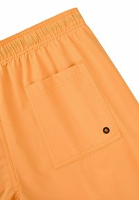 Short orange à taille élastique avec une poche arrière carrée ornée d’un petit œillet en métal noir.