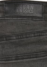 Crni traper tkanina s teksturiranom površinom. Ima kožni oznaku s brandom "URBAN CLASSICS DENIM FACTORY" na struku.