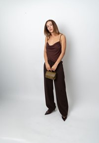 Camisole marron à encolure drapée, pantalon noir taille haute, et escarpins à bout pointu, tenant un sac à main texturé vert olive.