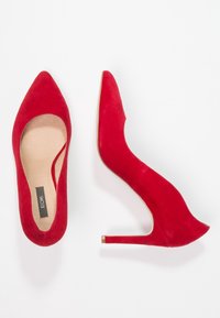 Röda mocka högklackade skor med spetsig tå och böjd design. Har en slät sula och en smal klack, med minimal hårdvara.