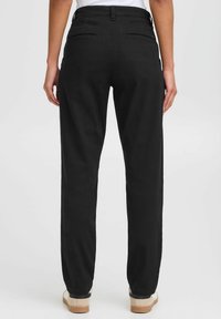 Pantaloni neri in cotone con design a gamba dritta, dotati di due tasche posteriori e una texture liscia. I pantaloni sono abbinati a sneakers beige.