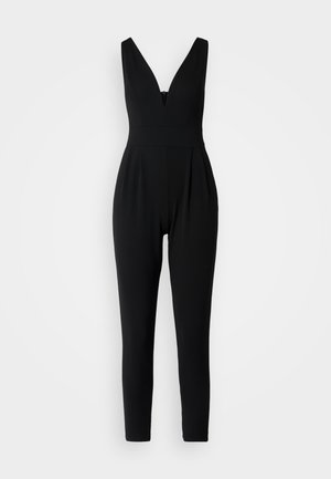 Črn kombinezon z globokim V-izrezom, prilegajočim bodijem in zoženimi hlačami. Ima zadrgo na hrbtu in naborke na pasu.