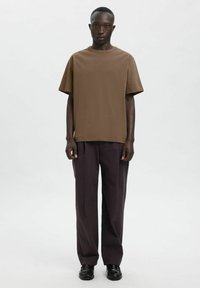 Pruun lühikeste varrukatega t-särk, millel on lõdvestunud lõige, kombineeritud tumedate pükste ja mustade kingadega. Ühtlane tekstuur ja lihtne disain ilma mustriteta.