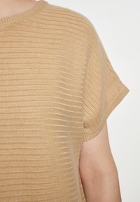 Maglione beige a coste con maniche corte, scollo rotondo e una texture morbida. Presenta righe orizzontali e una vestibilità comoda.