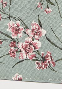 Motif floral sur fond texturé bleu clair. Comprend des fleurs roses avec des tiges et des feuilles vertes, détail de bordure cousue.