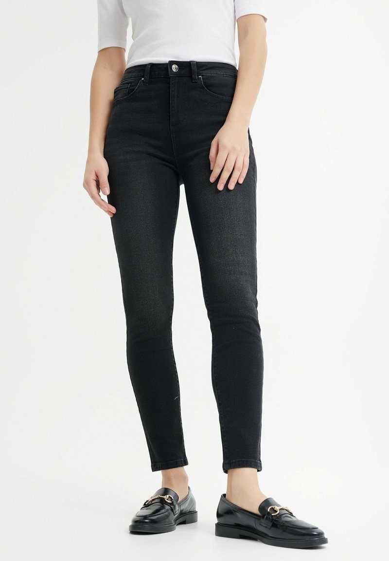 Czarne wąskie dżinsy wykonane z denimu, z wysokim stanem, pięcioma kieszeniami i subtelnym praniem. W połączeniu z czarnymi mokasynami.