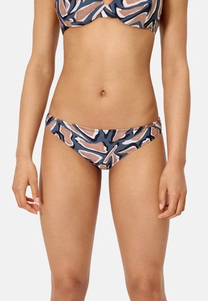 Mujer con bikini de partes inferior y superior con un patrón abstracto en marrón, azul marino y blanco, posando contra un fondo liso y claro.